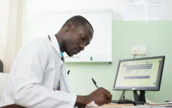 African researcher is seated at his desk. He holds a pen and is writing things down.