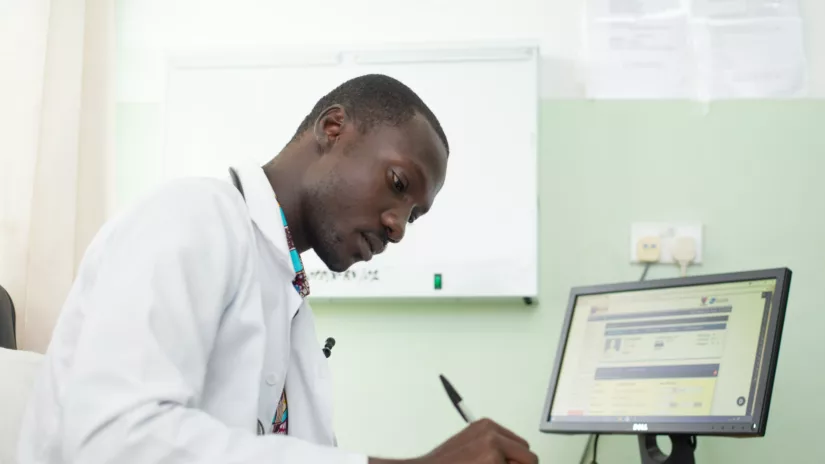 African researcher is seated at his desk. He holds a pen and is writing things down.