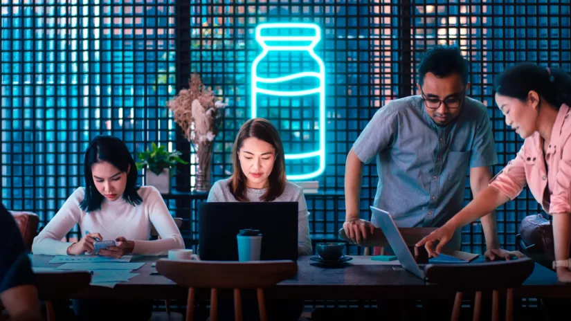 A team of people in an office at night time, with a glowing graphic of a medicine ampule behind them